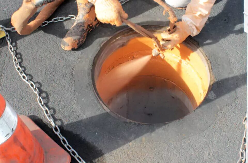Spray gun applying coating to a manhole