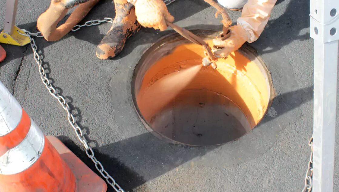 Spray gun applying coating to a manhole