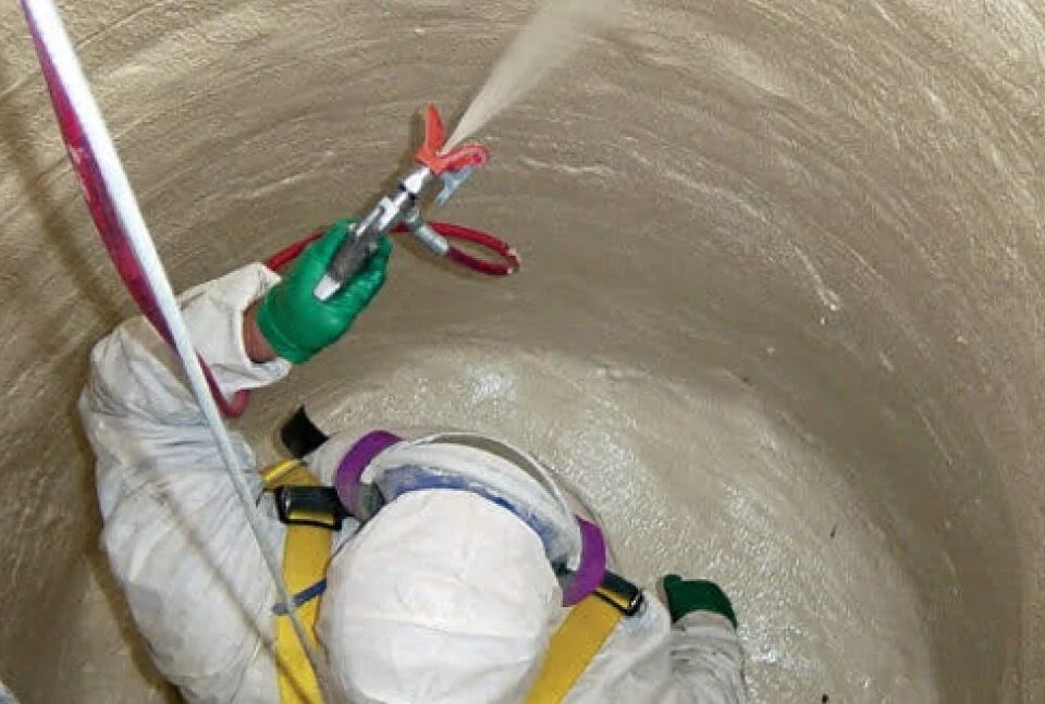 Applicator spraying a manhole interior from above